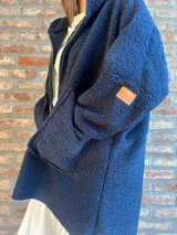 Campera de corderito color verde oscuro, con diseño holgado, cuello alto y manga larga. Presenta una etiqueta de cuero sintético en la manga.