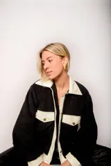 Campera de corderito negra con cuello, solapa, puños y bolsillos de cuero sintético color crema.