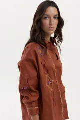 Camisa de lino color ladrillo, con mangas largas y bordados decorativos en el pecho y las mangas.