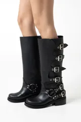 Botas de caña alta confeccionadas en cuero negro, con diseño de múltiples hebillas laterales y apliques metálicos decorativos en la zona del tobillo. Presentan un taco bajo cuadrado y punta redondeada.