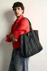 Bolso tipo shopper de algodón color negro, con asas superiores y tira de cuero con botón metálico para el cierre. Diseño amplio y versátil para uso diario.