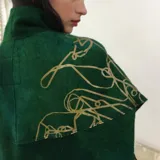 Poncho verde esmeralda de lana merino afieltrada con cuello alto y estampado dorado con diseño abstracto.
