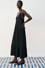 Vestido midi negro satinado con escote en pico, tirantes finos y detalle de lazada frontal. Presenta diseño de paneles fruncidos.
