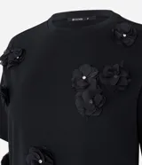 Remera Cortelle confeccionada en algodón, de corte ligeramente amplio, cuello redondo y manga corta. Presenta aplicaciones florales tridimensionales en relieve con detalles brillantes en el centro.