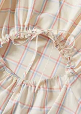 Vestido largo de algodón con diseño evasé, cuello redondo y sin mangas. Presenta un estampado de cuadros sutiles en tonos pastel y cuenta con una abertura en la espalda con cierre de lazo.