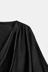 Blusa negra de satén con escote fluido, diseño drapeado en el frente y mangas largas anchas. Presenta un bajo asimétrico y una caída suave y elegante.