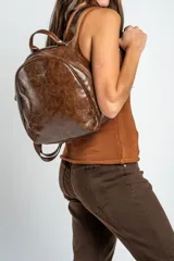 Mochila de cuero sintético marrón con efecto craquelado, asa superior y placa metálica frontal con el logo de la marca.