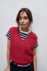 Chaleco tejido de punto color rojo con escote en V y terminaciones acanaladas en el cuello, sisas y dobladillo. Presenta un diseño sin mangas con sutiles líneas horizontales en el tejido.