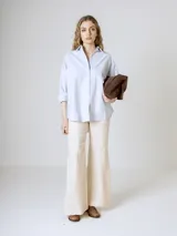 Camisa blanca de corte clásico, con cuello camisero y mangas largas con puños abotonados.