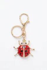 Llavero con dije de vaquita de San Antonio en color rojo y dorado, decorado con cristales brillantes en la cabeza y el centro del cuerpo.