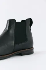 Bota tipo Chelsea de cuero negro con paneles elásticos laterales, suela de goma con detalle de vira en contraste y tirador trasero.
