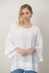 Blusa de lino color blanco, de corte amplio, con cuello redondo y mangas acampanadas con volados. Presenta detalles de alforzas horizontales y costuras decorativas en el ruedo.