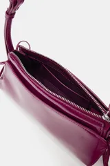 Bolso de hombro de material efecto acharolado en color fucsia, con diseño alargado, doble compartimento exterior y detalle de lazos en los laterales. Cuenta con doble asa de hombro ajustable y cierre superior con cremallera.