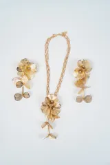 Set de joyería compuesto por un collar de cadena larga con dije floral y un par de aros colgantes a juego. Ambas piezas presentan un diseño de flores caladas en metal dorado con detalles de cristales en el centro.