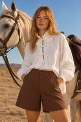 Blusa blanca de manga larga con cuello alto y volados, cierre frontal con lazos y diseño holgado.