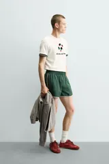 Camiseta de corte relajado confeccionada en piqué de algodón color crudo. Presenta cuello redondo, mangas cortas con ribetes a contraste y estampado frontal con el logo de Italia 90 FIFA World Cup.
