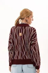 Buzo tipo polo de silueta relajada con cuello clásico y cartera con botones en el frente. Presenta un diseño tejido de ondas verticales en tonos bordó, celeste y crema.