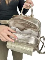 Mochila grande de cuero color dorado con bolsillo frontal con textura de piel de cocodrilo. Tiene asa de mano y correas ajustables para los hombros.