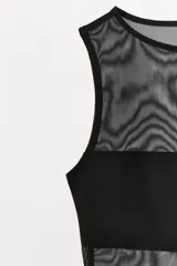 Body sin mangas de cuello redondo, confeccionado en una combinación de tul transparente y paneles de tela opaca a tono. Presenta un diseño ajustado con cierre inferior mediante botones a presión.