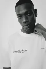 Remera blanca de algodón con cuello redondo y corte holgado. Presenta un estampado con texto en color negro en el frente.