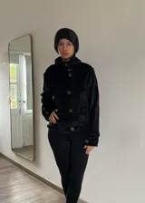 Campera corta de terciopelo negro con cierre frontal de botones dispuestos en diagonal y cuello alto abrigado. Cuenta con mangas largas y diseño sofisticado.