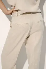 Pantalón sastrero color beige de tiro alto, confeccionado en mezcla de lino y lyocell. Presenta diseño de perneras rectas con pliegues frontales y traseros, bolsillos al bies y trabillas para cinturón.