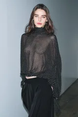 Blusa negra con estampado de lunares blancos, cuello redondo con lazadas y manga larga con puños ajustados. El bajo es ajustable con cordones.