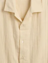 Camisa de manga corta color beige claro, con cuello cubano y cierre frontal de botones.