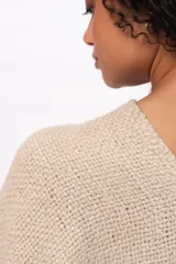 Ruana de tejido de punto en color arena, con diseño cruzado, escote en V y terminaciones con flecos en el ruedo. Incluye un parche de cuero con la marca Pura Lana en la parte frontal.