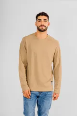 Buzo de manga larga con cuello redondo, confeccionado en tejido de punto con textura tipo waffle. Presenta un diseño minimalista con una pequeña etiqueta decorativa en el ruedo inferior.