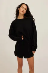 Sudadera negra de corte relajado, con cuello redondo, hombros caídos y costuras visibles en contraste. Cuenta con ribetes en cuello, puños y bajo.