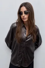 Camisa blanca de calce relajado con acabado satinado y brillo sutil, cuello clásico, cierre frontal con botones y mangas largas con puños.