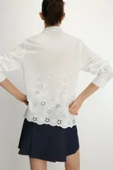 Camisa de manga larga en color blanco, confeccionada con detalles de bordados perforados a tono. Presenta un cuello tipo pañuelo y cierre frontal con botones.
