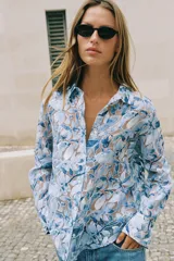 Camisa de manga larga con cuello solapa y cierre frontal de botones, confeccionada en tejido combinado semitransparente con estampado floral en tonos azules y blancos.