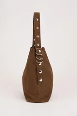 Bolso tipo shopper de gamuza marrón, con asa de hombro ajustable decorada con ojales metálicos plateados y hebilla lateral.