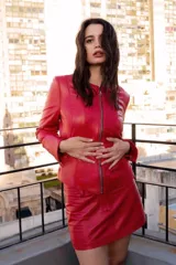 Chaqueta de cuero ovino color rojo, con cierre frontal de metal, cuello redondo y mangas largas con puños anchos ajustables mediante broches metálicos.