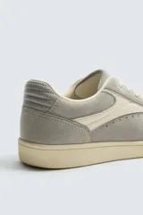 Zapatilla de estilo retro con cordones, confeccionada en una combinación de piezas de gamuza y material sintético. Presenta suela de goma a contraste y diseño de paneles laterales.