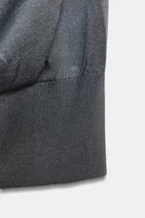 Top de punto color gris oscuro con cuello halter y escote drapeado pronunciado. Presenta un acabado con hilo metalizado y un borde inferior de punto acanalado.