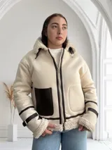 Chaqueta color crudo con interior de piel sintética color beige, cierre frontal con cremallera y un bolsillo de cuero marrón en el pecho.
