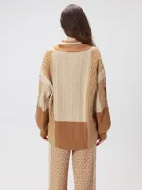 Cardigan oversize de tejido de punto grueso con diseño de bloques de color en tonos tierra. Presenta cuello en V, cierre frontal con botones, mangas largas con terminación abullonada y parches decorativos en el pecho y hombro.