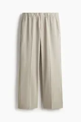 Pantalón de corte relajado en tejido suave, color beige, con cintura elástica, pliegues frontales, bolsillos laterales y bolsillos traseros ribeteados.