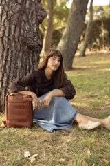 Matera mochila unisex de cuero marrón, con diseño estructurado, bolsillo frontal con cierre, asas superiores y correas ajustables.