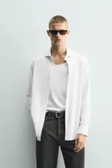 Camisa de manga larga color verde oscuro, con cuello italiano abierto y cierre frontal de botonadura. Presenta un calce ajustado (slim fit) y puños con botón.