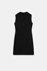 Vestido corto negro con brillo, cuello redondo y manga sisa. Presenta un detalle de aplicación de hilo metalizado y bajo recto.