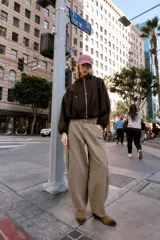 Chaqueta estilo bomber de corte oversize en color marrón oscuro, confeccionada en tejido suave. Presenta capucha con cordones ajustables, cierre frontal con cremallera, mangas largas con puños elásticos y bolsillos delanteros de vivo. El bajo cuenta con detalle de pliegues.