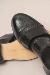 Zapato tipo monk strap con aberturas laterales, confeccionado en cuero vacuno metalizado color bronce. Presenta detalles de perforaciones estilo brogue en la puntera y el talón, y doble hebilla metálica en el empeine.