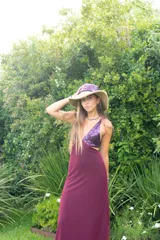 Vestido largo con estampado tie-dye en tonos violeta y fucsia, escote en V con detalles bordados dorados, cut-outs laterales bajo el busto y tirantes finos que se cruzan y atan en la espalda.