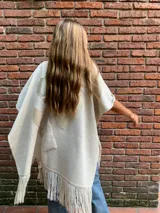 Ruana color crema de tejido de punto fino en lana con detalles en cuero y flecos.