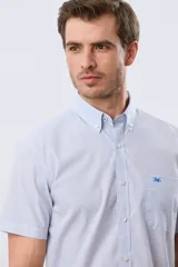 Camisa de manga corta a rayas celestes y blancas, con cuello abotonado, bolsillo frontal en el pecho con logo bordado y cierre frontal de botones.