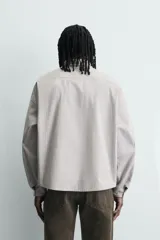 Camisa de corte boxy fit confeccionada en tejido de algodón con diseño de rayas verticales. Presenta cuello solapa, manga larga con puños abotonados y cierre frontal de botones. El frente destaca por bordados y estampados a contraste.